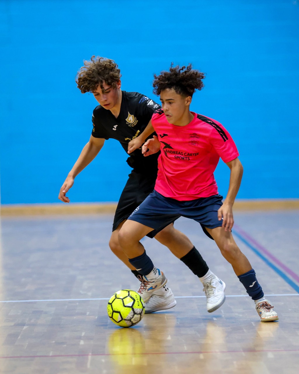 Ethan Chibambo in action, shielding the ball from an opponent on an indoor futsal court.